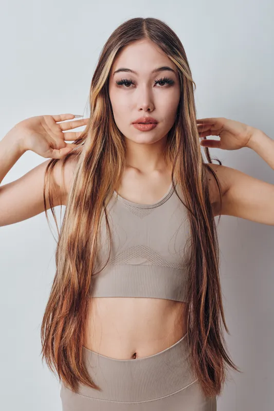 Young woman with long straight hair wearing a beige crop top and matching bottoms posing against a plain light background. Beauty, fashion, and casual style portrait.