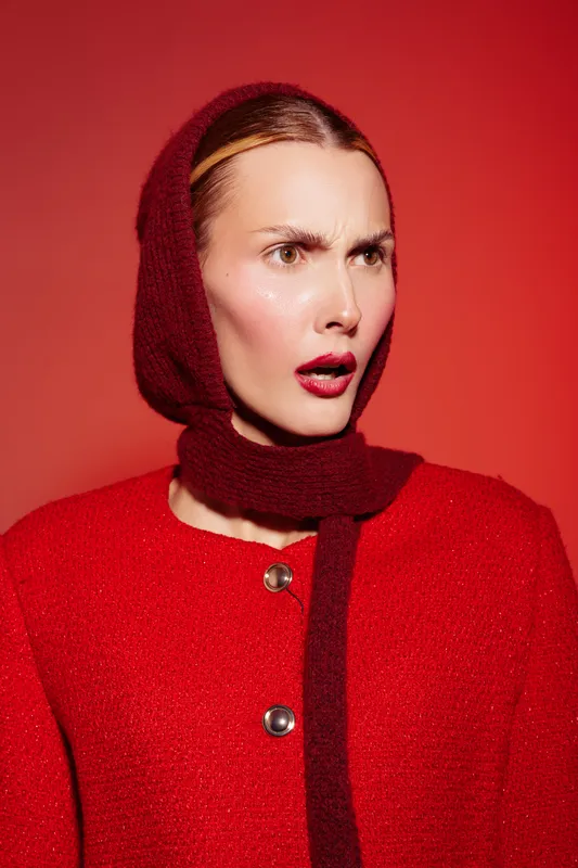 Surprised woman in red woolen coat and matching scarf looks shocked with open mouth on red background. Concept of emotion, fashion, winter style, and expressive portrait.