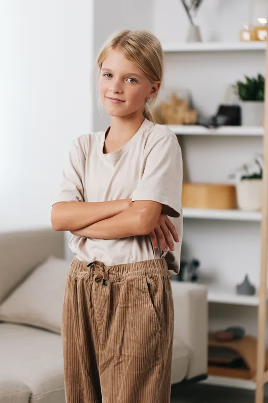 Authenticity shines as a young girl stands with arms crossed in a relaxed home setting, hinting at playful study moments and a daily lifestyle framed by a subtle school theme.