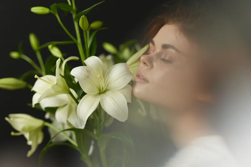 Young woman with closed eyes enjoying the scent of white lilies, exhibiting calmness, elegance, and natural beauty, perfect for wellness or floral themes