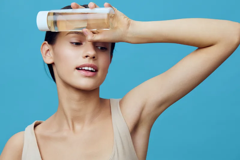 Young woman holding a skincare bottle, showcasing natural beauty against a vibrant blue background, embodying self care and wellness concepts