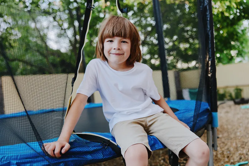 Happy boy sitting on a trampoline, enjoying outdoor playtime in summer. His cheerful expression adds to the joyful atmosphere of childhood fun and freedom.