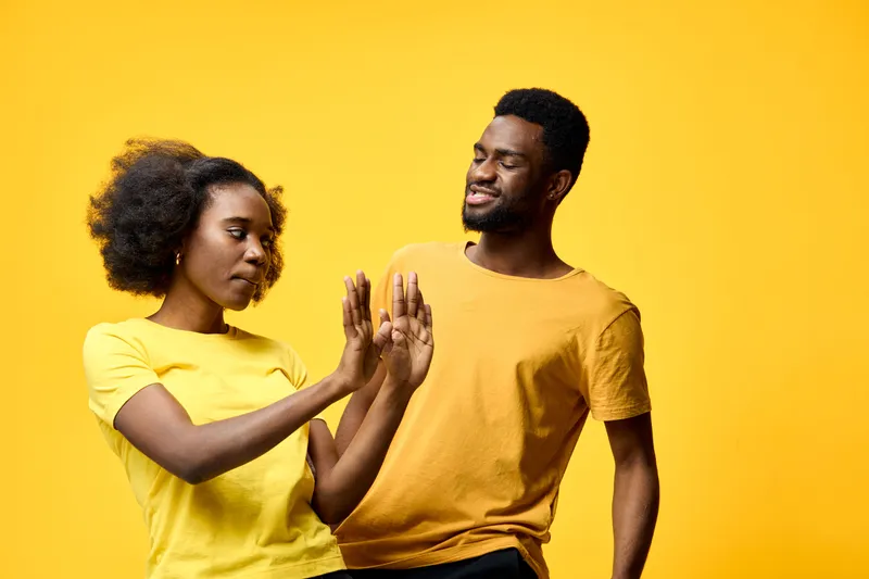 A joyful couple interacting playfully against a bright yellow background, showcasing vibrant emotions and casual summer attire