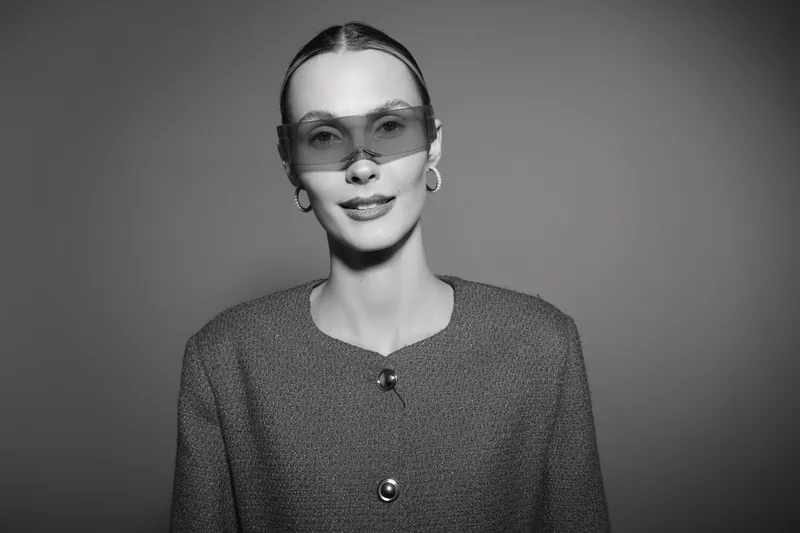 Portrait of a young white woman with pale skin and slicked hair wearing oversized sunglasses and a textured jacket in a studio. Concept for fashion, style, and modern elegance.