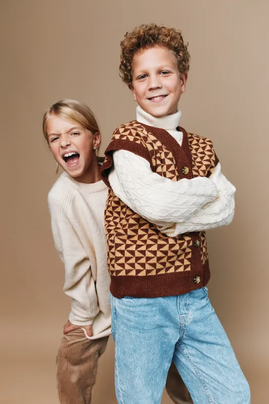 Authentic scene of children at play, featuring a joyful pair in cozy knitwear and denim as they pose with confidence, capturing genuine energy and friendship.