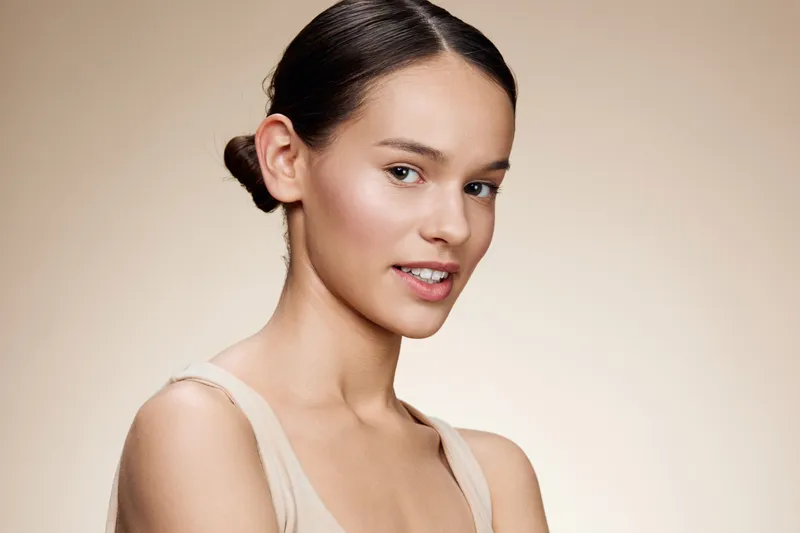 Portrait of an elegant model with a natural makeup look, showcasing healthy skin and subtle smile against a warm beige background, perfect for beauty and skincare concepts
