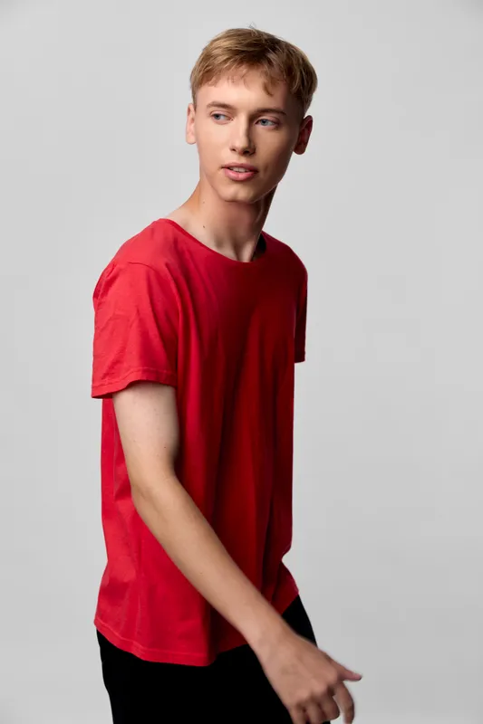 Young man wearing a red shirt in a studio setting, casual fashion shoot with a relaxed pose, natural expression, and modern style against a clean background.