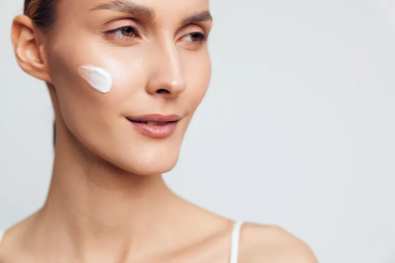 Woman face cream closeup, applying white moisturizer on cheek, studio portrait on light background, skincare and beauty concept, wellness and care routine, soft studio lighting, calm mood