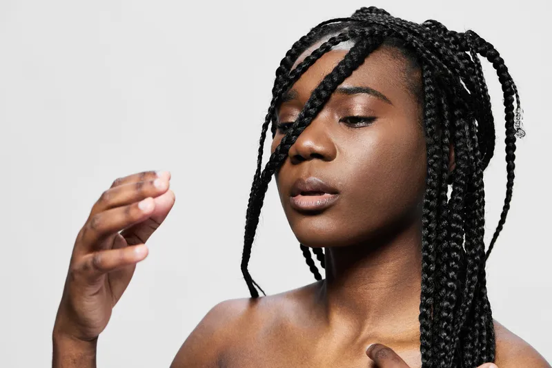 Young model with braided hair expressing confidence against a minimalist background, showcasing beauty, elegance, and self love in a professional photoshoot