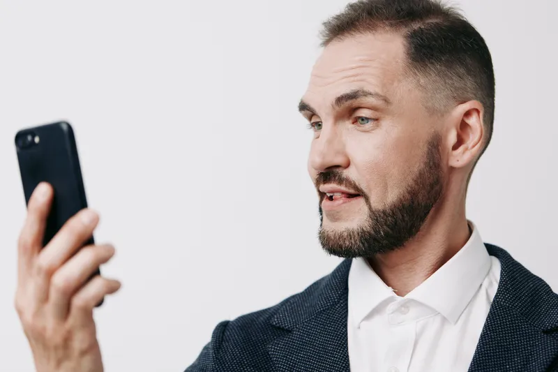 A professional business man on a colored isolated background, sharing a thoughtful moment while looking at a smartphone, conveying confidence and focus.