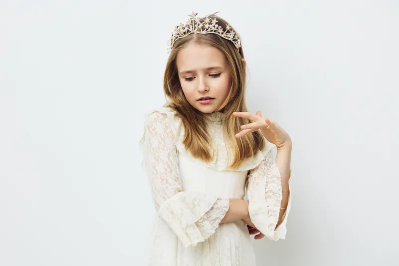 A girl in a white dress and crown expresses gentle emotions against a light background, showcasing innocence and elegance, perfect for children s themes