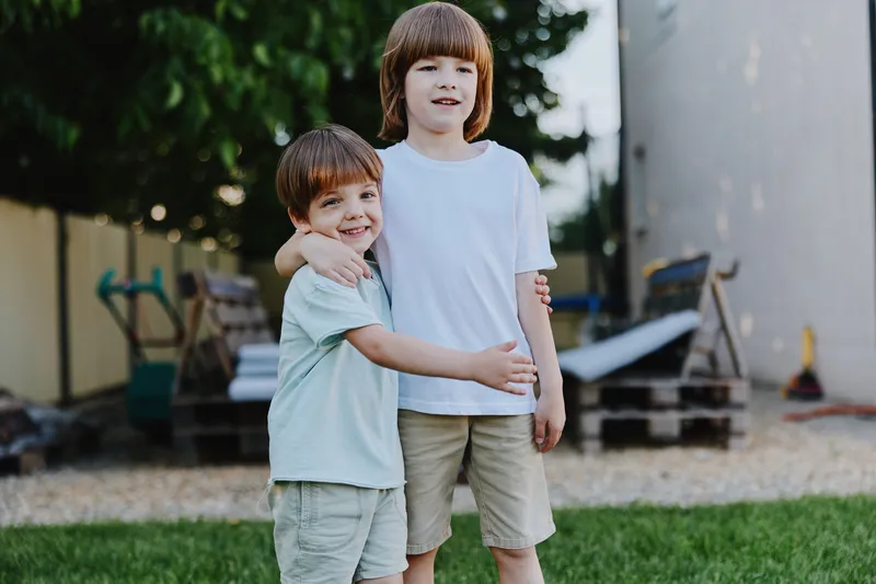 Two cheerful boys enjoying a sunny day outdoors, showcasing a playful moment with warm smiles and casual summer clothing in a bright garden backdrop.