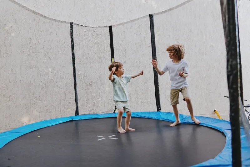 Energetic children jumping on a trampoline, surrounded by a safe net, enjoying their playful moments during a sunny day. Perfect for family fun concepts.
