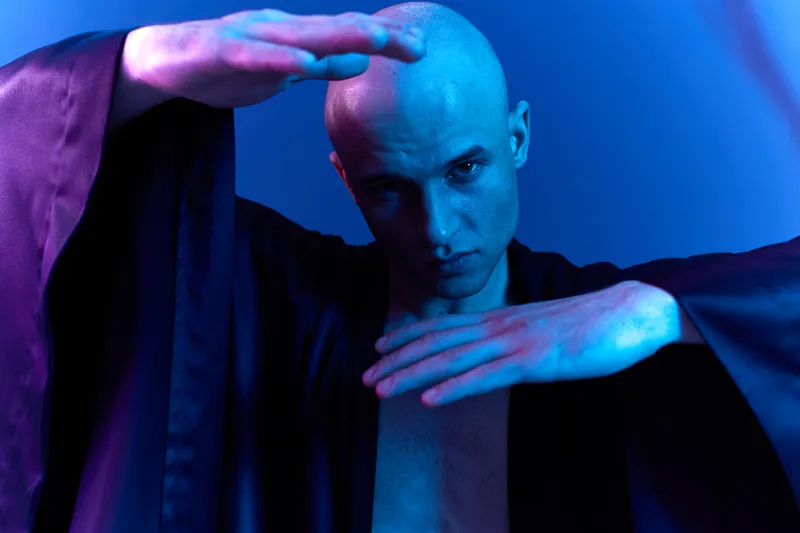 Striking man in a dramatic pose, showcasing artistry with illuminated colors in a mesmerizing black and white image. A captivating visual experience awaits viewers.
