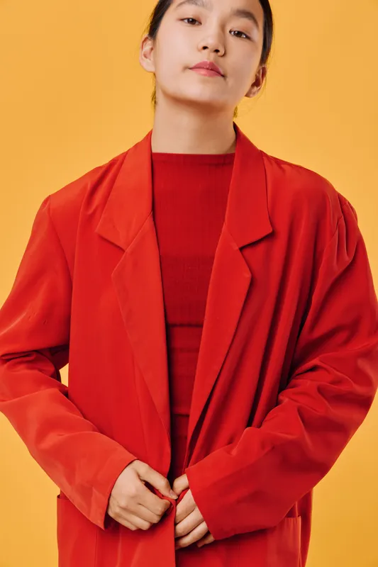 Young woman wearing red oversized blazer and matching shirt posing confidently on yellow background. Closeup portrait with casual style and minimal makeup showing modern fashion vibes.