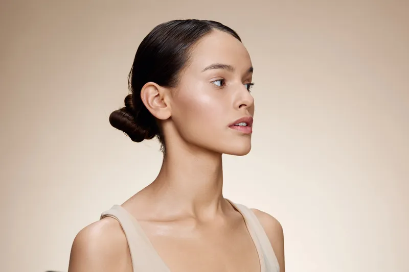 Elegant young woman with a clean makeup look, showcasing healthy skin in a neutral toned background, emphasizing natural beauty and simplicity