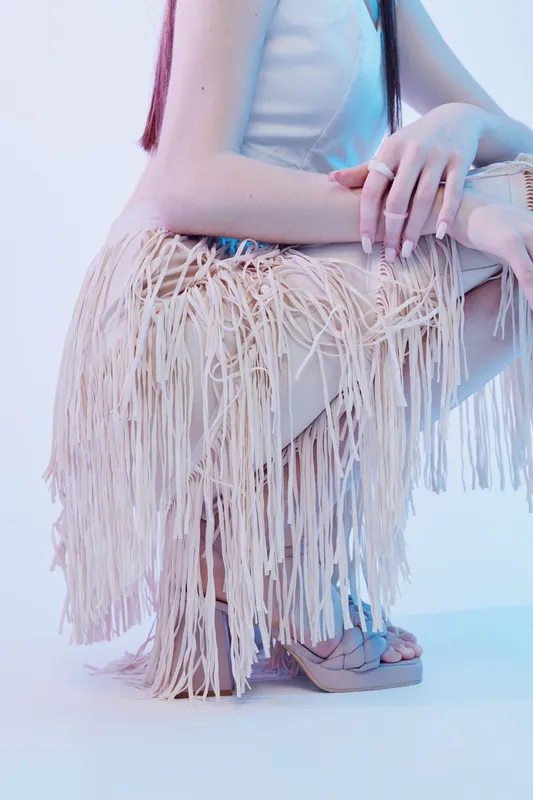Woman beauty fashion concept with a close-up of a model wearing a fringed skirt and platform sandals. Soft lighting highlights texture and style in a studio setting.