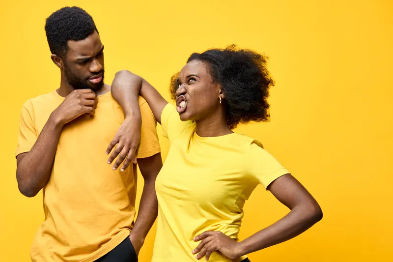 African American couple expressing playful disagreement in matching yellow shirts against a vibrant yellow background, showcasing emotions of frustration and humor