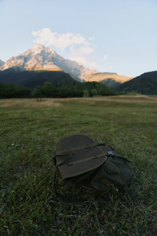 Backpack lying on green grass in front of a mountain with clear sky. Concept of hiking, nature, adventure, and outdoor lifestyle during daytime.
