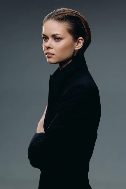 Serious young woman in black sweater with braided hair posing against gray background