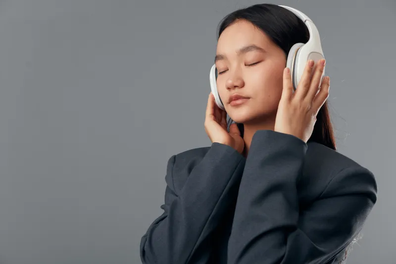 Young woman wearing headphones with eyes closed enjoying music, relaxation and calm in studio environment. Asian female listening to audio with focus and peaceful expression on face.