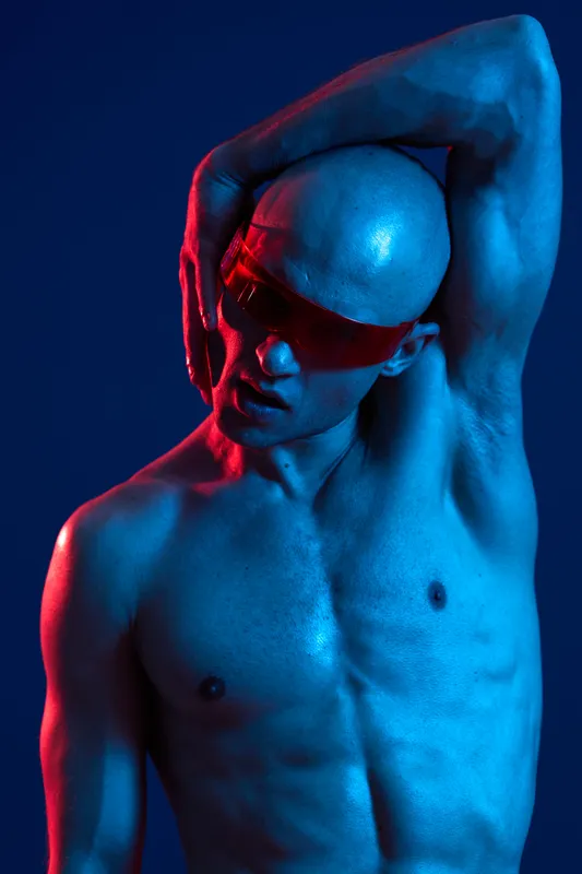 Athletic man posing dramatically with a striking blue and red lighting effect, showcasing a unique fashion style and confident expression.