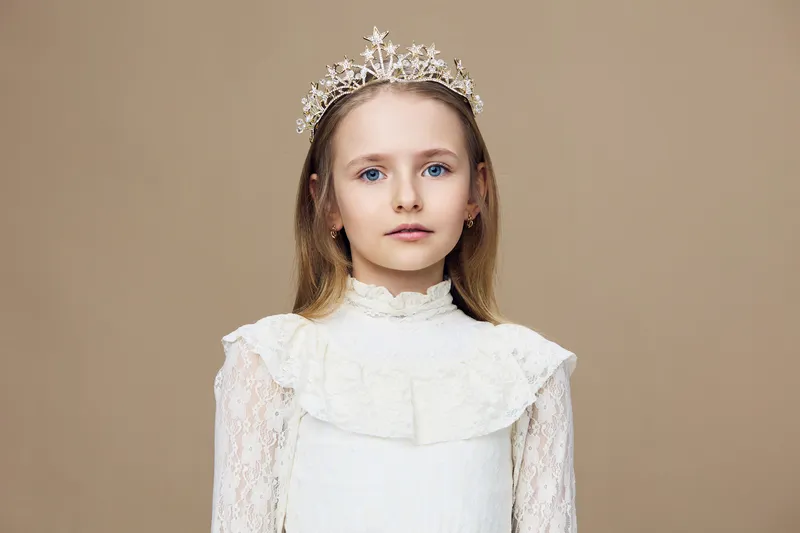 Young girl in a white dress and tiara, exuding elegance and grace, set against a soft beige background, perfect for celebrations or portrait sessions