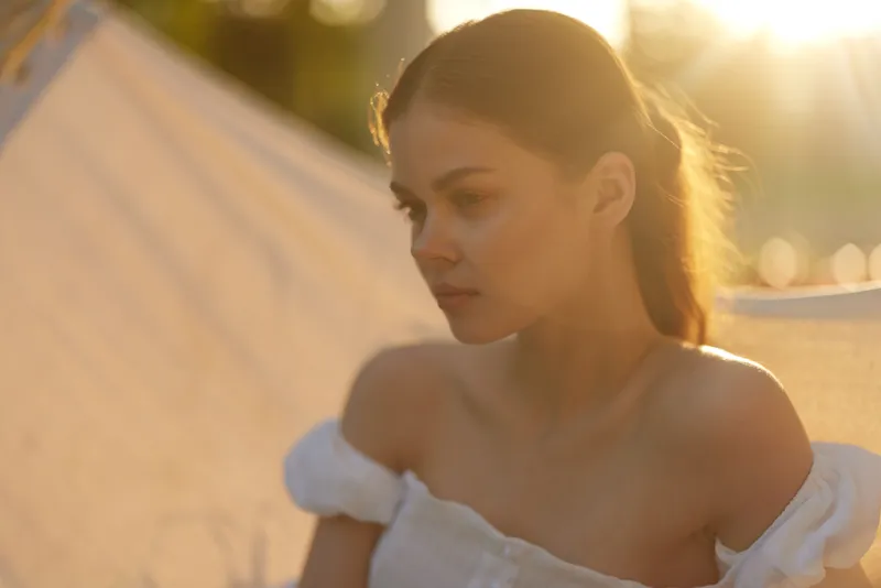 Serene young woman with long hair in a white dress, embodying tranquility and beauty during sunset, evoking emotions of peace and reflection