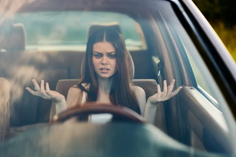 Young woman displaying frustration while sitting in a car, expressing confusion and uncertainty.