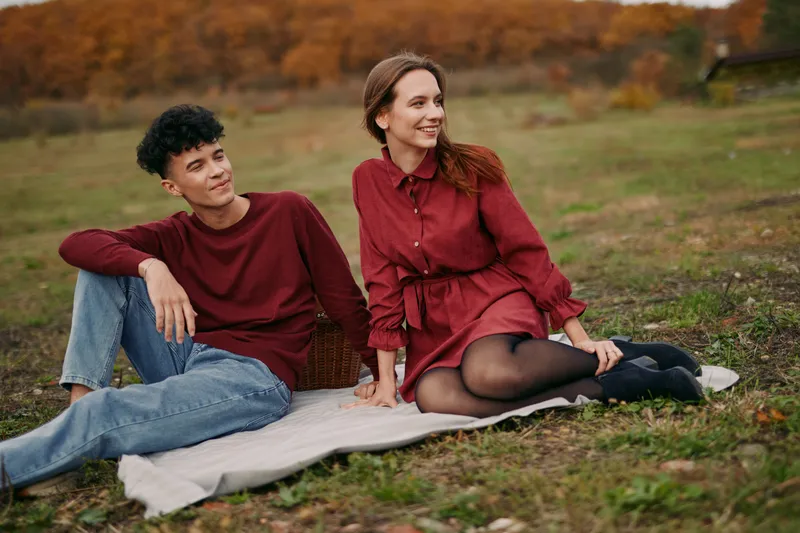 An authentic candid moment captures two people relaxing on a blanket in a sunlit autumn park, presenting genuine connection and a natural, unscripted mood.
