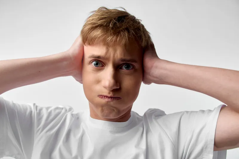 Frustrated man pulls his ears with a puzzled expression, white t shirt, studio close up, dramatic lighting, awkward moment, emotion and tension in a single frame