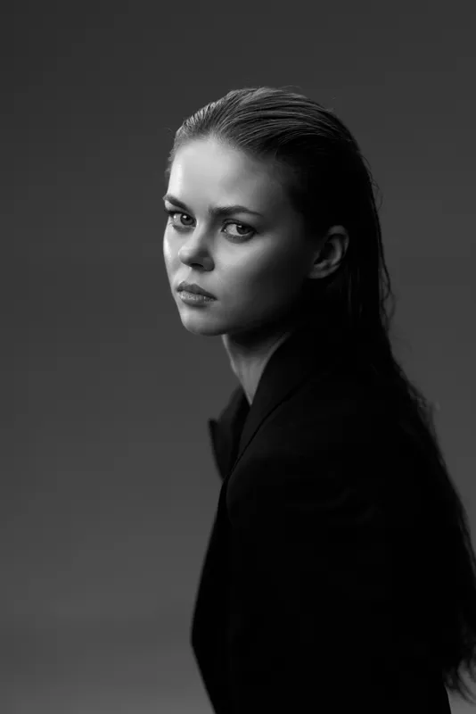 Black and white portrait of a serious woman with wet hair, wearing a dark jacket against a dark background