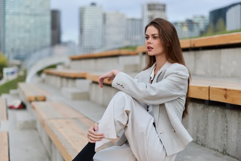 Confident businesswoman in stylish suit, seated outdoors, expressing determination and poise in an urban environment, ideal for professional themes and corporate visuals.