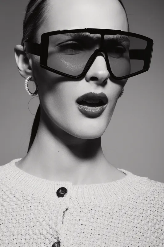 Close-up of a fair skinned Caucasian woman wearing oversized glasses and knitted sweater with hoop earrings in black and white photo.