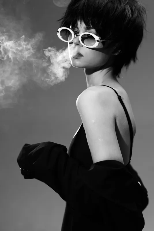 Black and white portrait of a stylish woman with short hair wearing sunglasses blowing smoke