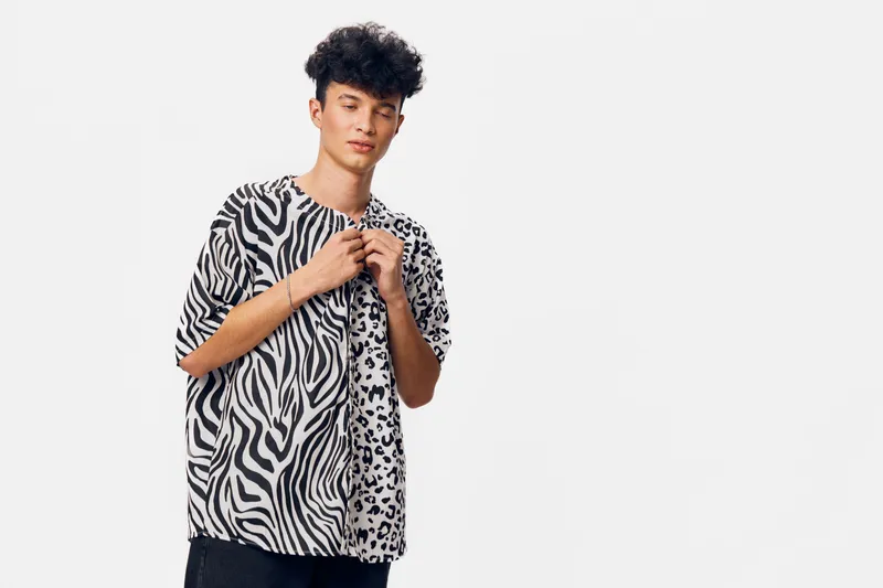 young man wearing animal print shirt with relaxed posture against plain white background in casual style, afro hairstyle, minimalistic studio setting