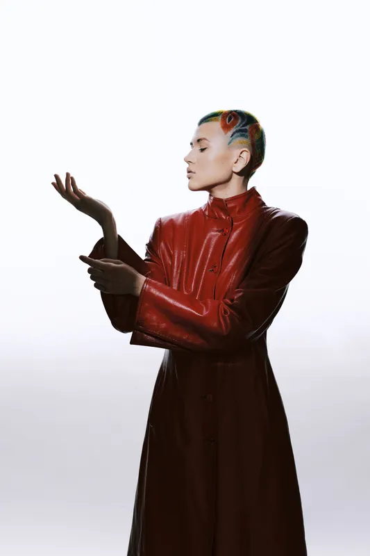 bald woman with colorful hair art wearing a red leather coat, standing in profile with a minimalist white background, modern fashion style, creative expression