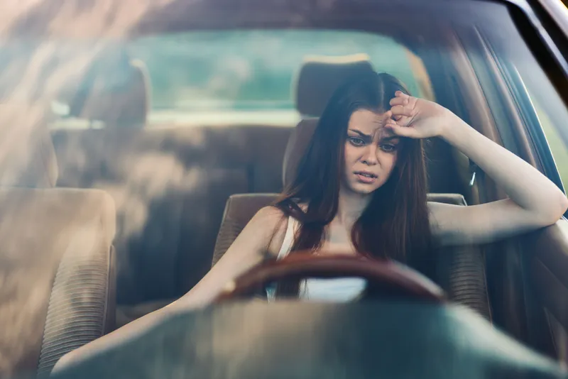 Young woman feeling stressed in a car, showcasing frustration and anxiety with hand on forehead, creating an emotional and relatable atmosphere.