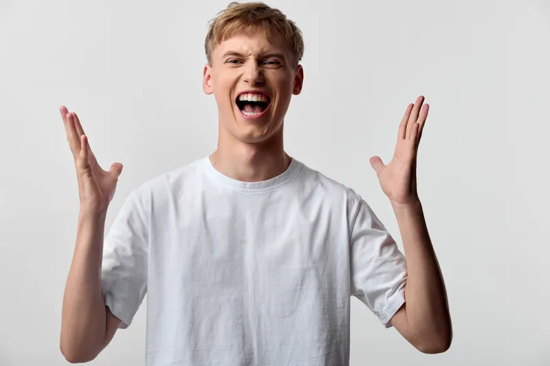 Energetic young man in a white shirt raises hands in excitement, bright smile and dynamic energy, suitable for lifestyle, celebration and motivation contexts and positive wellbeing imagery