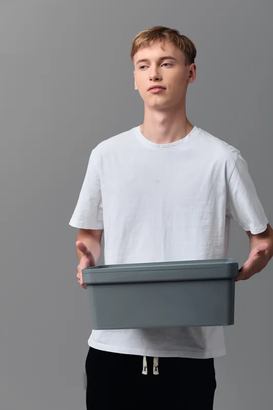 Young man holding a gray storage box for delivery and packaging, simple studio shot with neutral background, illustrating logistics and shipping preparation