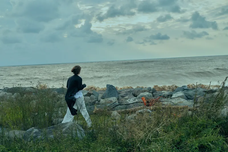 Coast, walking, man, ocean, shore, rocky path, overcast sky, casual outdoor scene, windy mood, travel moment