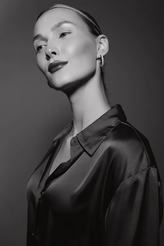 Elegant caucasian woman with light skin posing in silk shirt in studio, black and white fashion portrait with soft lighting.