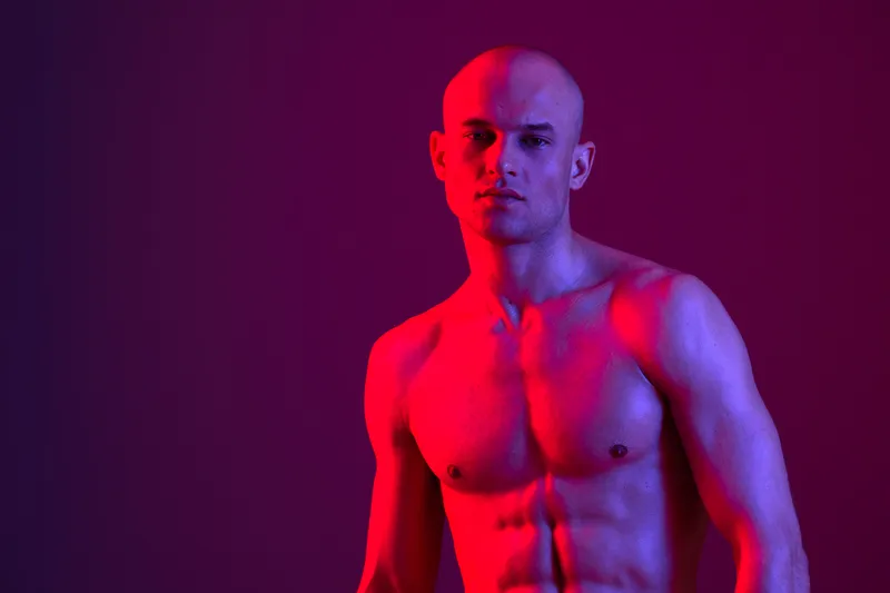 A striking portrait of a man with a strong physique, captured in vibrant colored light, showcasing bold contrasts and dynamic expressions. Perfect for fitness themes or masculine art.