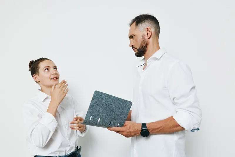 A professional business man stands with a notebook while a colleague looks up, against a clean isolated white background; calm, confident emotion highlights collaboration, leadership, and thoughtful