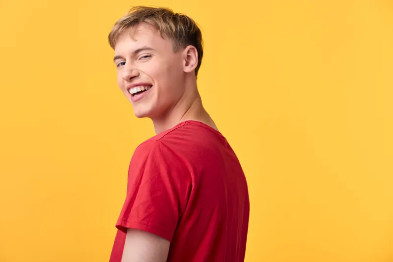 Smiling young man in a red t shirt against a vibrant yellow backdrop, conveying positivity, energy and casual charm for lifestyle, fashion and promotional photography.
