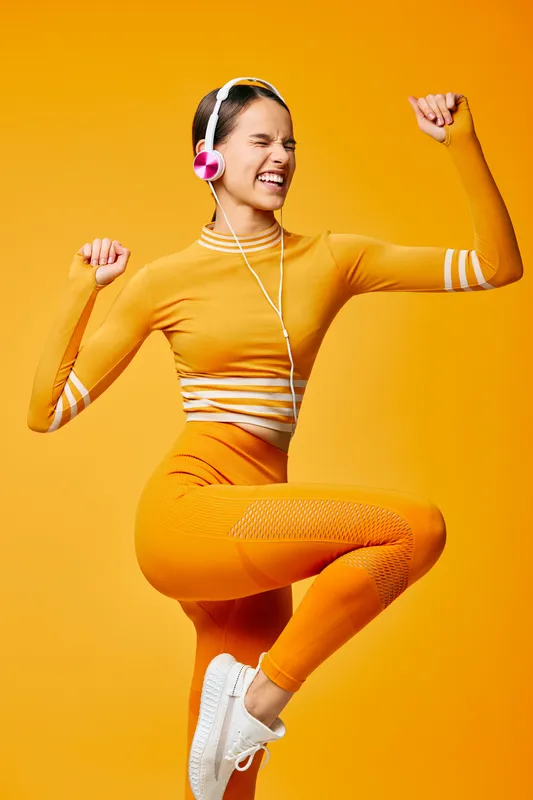Fitness woman in orange athletic wear dances with headphones, exuding energy and vibrant movement. A dynamic sport lifestyle image perfect for active campaigns.