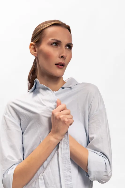 Concerned young woman wearing a light shirt looks to the side with worried expression, holding her hands close to her chest. Studio portrait on white background, concept of anxiety and fear.