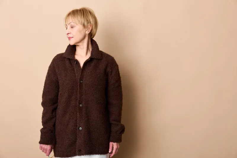 Woman portrait blonde sweater studio beige relaxed winter mood, mature female standing calmly, neutral pose, warm knit cardigan on plain background, soft light