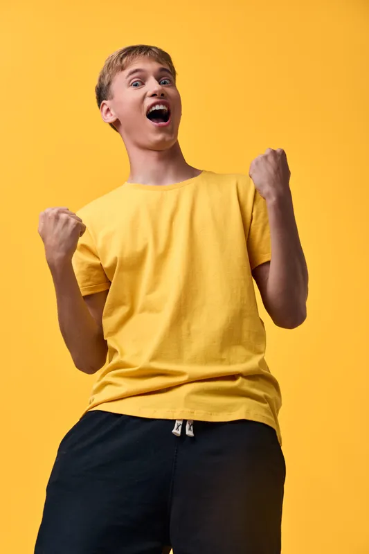 Energetic man in a yellow t shirt celebrates victory with raised fists against a bright yellow backdrop, dynamic pose and joyful expression conveying celebration, motivation and bold momentum