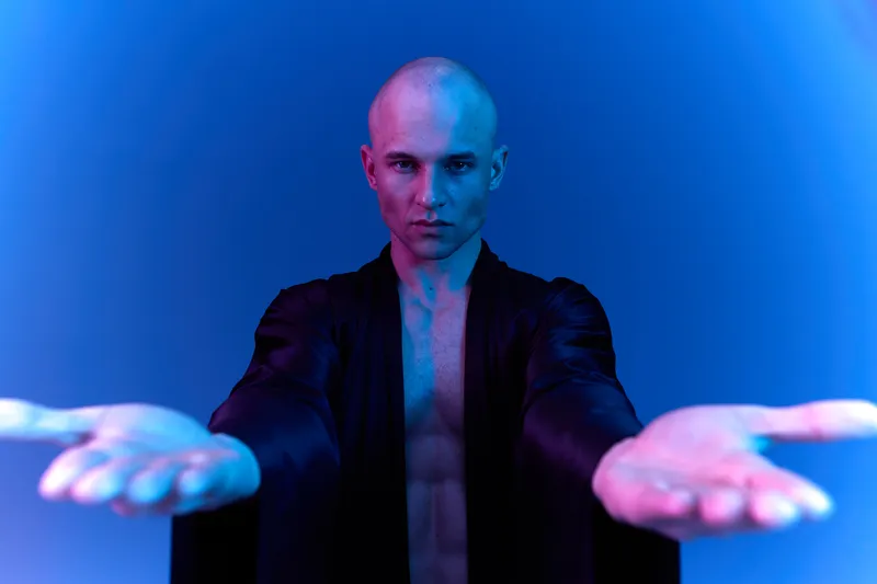 Charismatic man presenting with open hands, showcasing a striking display against a vibrant blue background. Captivating aura exudes confidence and mystery.
